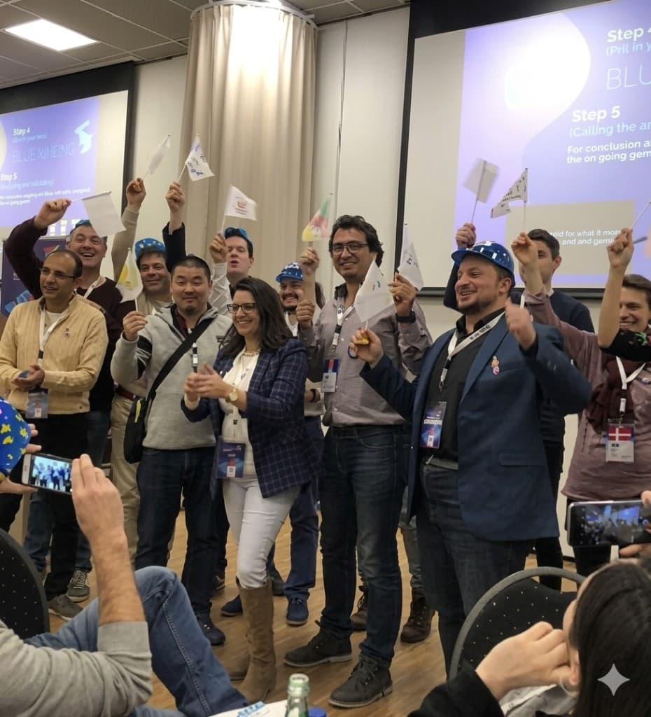 Diverse professionals celebrating together on stage after a workshop, holding small flags while colleagues photograph the moment.